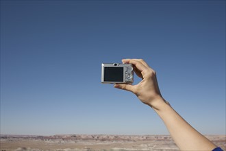 Hand of woman holding camera up against blue sky. Photo : Winslow Productions