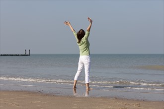 Woman on beach with arms raised. Photo: Jan Scherders