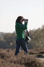 The Netherlands, Veluwezoom, Posbank, Woman in countryside looking through binoculars. Photo: Jan