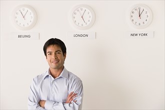 Portrait of businessman with world clocks behind. Photo : Rob Lewine