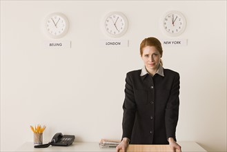 Portrait of businesswoman with world clocks behind. Photo: Rob Lewine