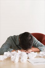 Businessman sleeping at desk with crumpled paper balls. Photo : Rob Lewine