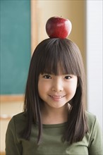 Portrait of girl (6-7) balancing apple on head. Photo: Rob Lewine