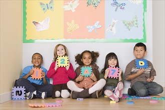 Children (6-7) sitting and holding letters in classroom. Photo : Rob Lewine