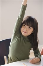 Girl (6-7) raising hand in classroom. Photo : Rob Lewine