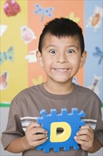 Smiling boy (6-7) holding letter D. Photo : Rob Lewine