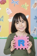 Smiling girl (6-7) holding letter R. Photo : Rob Lewine