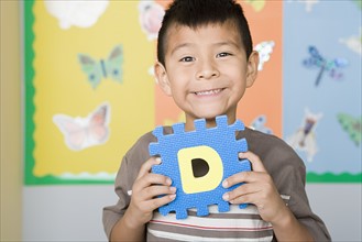 Boy (6-7) holding D letter in classroom. Photo : Rob Lewine