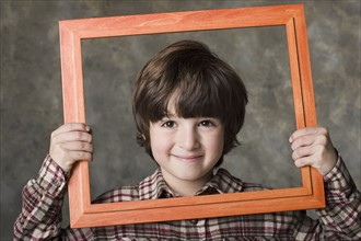 Smiling boy (6-7) looking through frame, studio shot. Photo : Rob Lewine