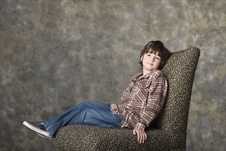 Portrait of boy (6-7) sitting on chair, studio shot. Photo: Rob Lewine