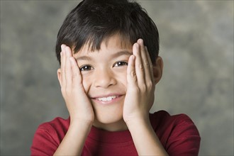 Portrait of smiling boy (8-9) with hands on face, studio shot. Photo : Rob Lewine