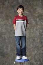 Portrait of smiling boy (8-9) standing on stool, studio shot. Photo : Rob Lewine