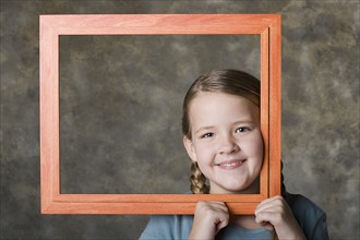 Portrait of smiling girl (8-9) holding frame, studio shot. Photo : Rob Lewine