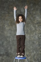 Portrait of smiling girl (8-9) with arms raised, studio shot. Photo : Rob Lewine