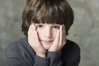 Portrait of boy (6-7) with face in hands, studio shot. Photo : Rob Lewine