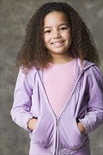 Portrait of smiling girl (8-9) with hands in pockets, studio shot. Photo : Rob Lewine