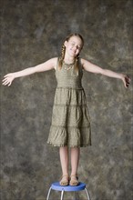 Portrait of smiling girl (8-9) standing on stool, studio shot. Photo : Rob Lewine