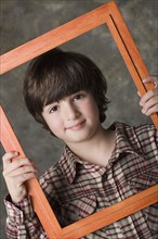 Portrait of boy (6-7) looking through frame, studio shot. Photo : Rob Lewine