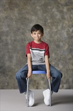 Portrait of smiling boy (8-9) sitting on stool, studio shot. Photo : Rob Lewine