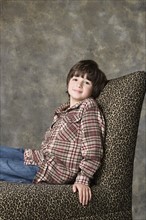 Portrait of boy (6-7) sitting on chair with animal print, studio shot. Photo : Rob Lewine