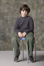 Smiling boy (6-7) sitting on chair, studio shot. Photo : Rob Lewine