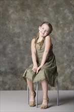Portrait of smiling girl (8-9) sitting on stool, studio shot. Photo : Rob Lewine