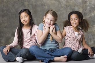 Portrait of three smiling girls (8-9) sitting together, studio shot. Photo : Rob Lewine