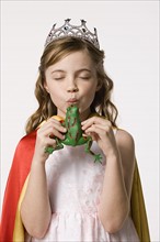 Studio portrait of girl (8-9) wearing princess costume and kissing toy frog. Photo: Rob Lewine