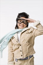 Studio portrait of saluting girl (8-9) wearing aviator's cap and flying goggles. Photo : Rob Lewine