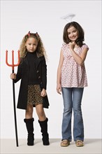 Studio portrait of two girls (8-9) wearing Halloween costumes with trident and halo. Photo: Rob