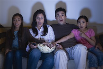 Parents with two daughters (8-9, 10-11) watching tv on sofa. Photo : Rob Lewine