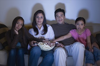 Family with two daughters (8-9, 10-11) watching tv on sofa. Photo: Rob Lewine