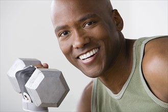 Portrait of smiling young man lifting dumbbell. Photo : Rob Lewine