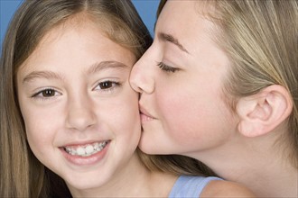 Portrait teenage girl (14-15) kissing younger sister. Photo: Rob Lewine