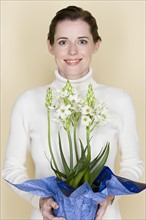 Portrait of smiling woman holding flowers, studio shot. Photo : Rob Lewine