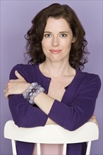 Portrait of smiling woman sitting on chair with purple background, studio shot. Photo : Rob Lewine