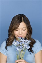 Portrait of woman smelling flowers on blue background, studio shot. Photo : Rob Lewine