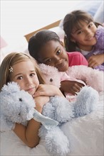 Portrait of three smiling girls (10-11) with puppets in bed. Photo : Rob Lewine