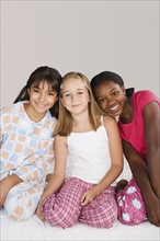 Portrait of three girls (10-11) sitting on bed at slumber party. Photo: Rob Lewine