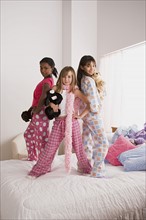 Portrait of three girls (10-11) standing on bed at slumber party. Photo: Rob Lewine