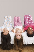 Portrait of three girls (10-11) lying on bed with heads down . Photo : Rob Lewine