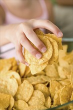 Close up of girl's (10-11) hand taking potato chips from bowl. Photo : Rob Lewine