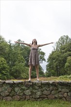USA, New Jersey, Happy woman standing on stone wall on field. Photo: Tetra Images