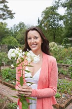 Portrait of smiling woman holding white flowers in garden. Photo: Tetra Images