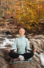 Woman meditating by stream in forest. Photo : Tetra Images