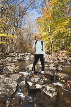 Female hiker standing on rock in stream in forest. Photo : Tetra Images