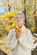 Smiling woman holding leaves in Autumn forest. Photo : Tetra Images
