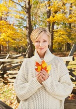 Portrait of smiling woman holding leaves in Autumn forest. Photo: Tetra Images