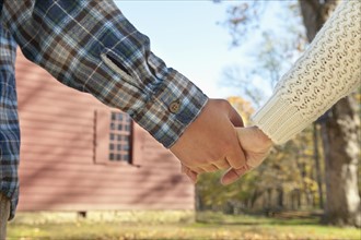 Close-up of couple holding hands in front of cottage house. Photo: Tetra Images