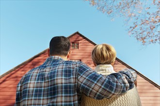 Rear view of couple facing cottage house. Photo: Tetra Images